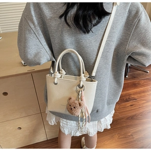 Detail of white pleated leather bucket bag with teddy bear charm and striped strap