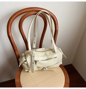 Detail of cream yellow glossy leather handbag with silver zippers on a vintage chair