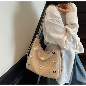 Detail of a beige tote bag with black and white butterfly charms and adjustable strap