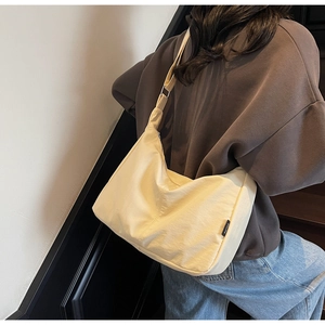 Detail of cream canvas hobo bag with adjustable strap and side brand label shown on model