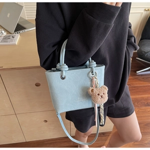 Detail of light blue bucket bag with knotted handle and cute brown teddy bear charm