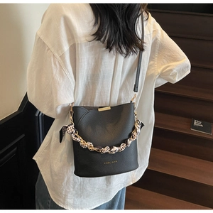 Détail du sac seau en cuir noir avec garniture dorée et foulard en soie sur la poignée