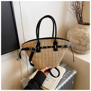 Close-up of woven straw tote bag featuring black leather trim and decorative metal buckles