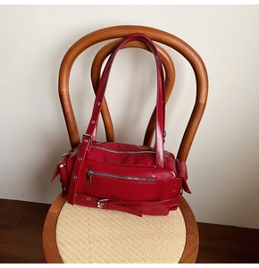 Detailed view of red glossy leather shoulder bag with silver buckles on a vintage chair