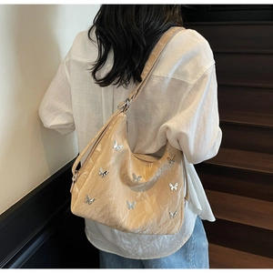 Detail of apricot pleated leather shoulder bag with silver butterfly charms on model