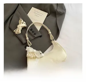 Detail of cream hobo bag with lychee texture and pearl lace bow charm on grey blazer