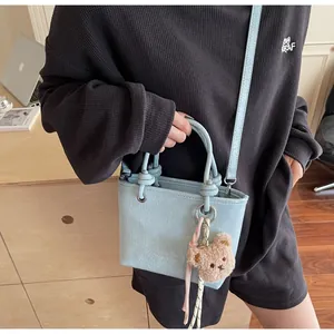 Detail of light blue mini tote bag with wrinkled texture, plush bear charm and long strap