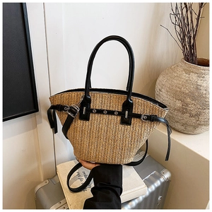 Detailed view of woven straw tote bag featuring black leather buckle and handle