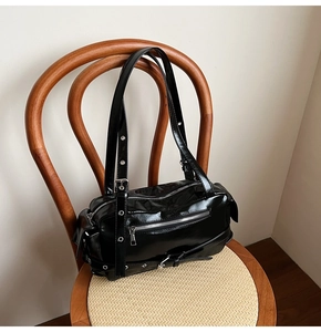 Detail of black glossy leather pillow bag featuring motorcycle style zips and buckles