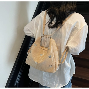 Detail of beige convertible backpack with silver butterfly accents on textured fabric