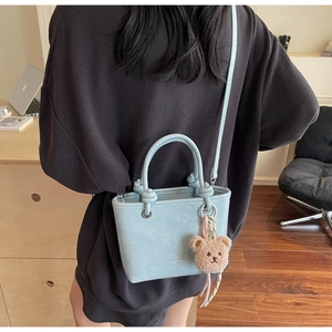 Light blue faux leather mini tote bag with bear charm shown in a cozy home lifestyle setting