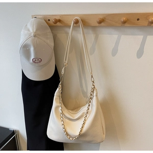 Detail of cream pebbled leather tote bag featuring gold chain and adjustable shoulder strap