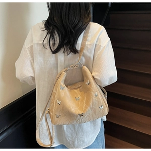 Detail view of beige hobo bag with pleated texture and silver butterfly metal ornaments