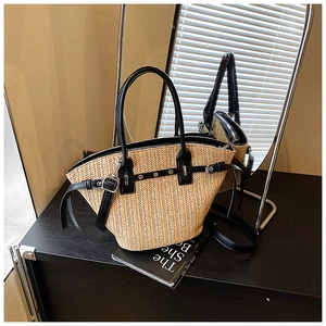 Detail of woven straw tote bag featuring black leather straps and silver metal hardware accents