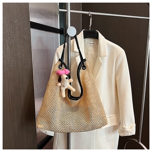 Detail of woven straw tote bag featuring black leather handles and plush dog charm