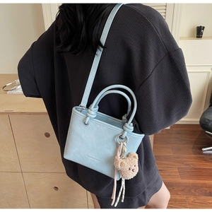 Detail of light blue crossbody bag with knot handle and cute bear charm accessory