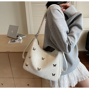 Detail of white textured leather underarm bag featuring silver metal butterfly accents