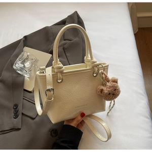 Close-up of beige textured leather handbag with brand logo and cute brown teddy bear charm