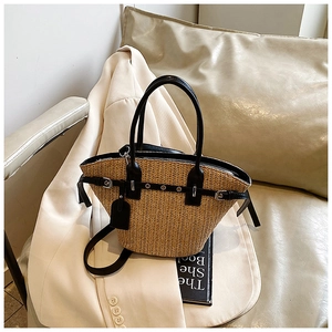 Detailed view of woven straw tote bag with black leather straps on a cream sofa