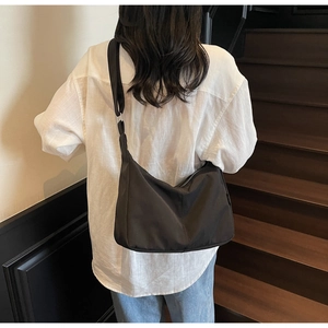 Minimalist black canvas dumpling bag with wide shoulder strap worn by a model in a stairwell