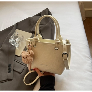 Detail of off-white pleated leather bucket bag with teddy bear charm on white bedding