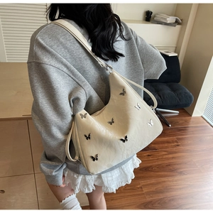 Detail of beige faux leather shoulder bag with silver butterfly buckles on model