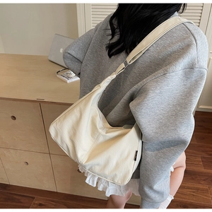 Detail of a cream soft leather shoulder bag showing the wide strap and natural draping texture