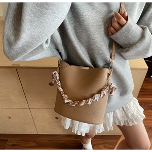 Detail of brown leather bucket bag featuring a silk scarf wrapped metal chain strap