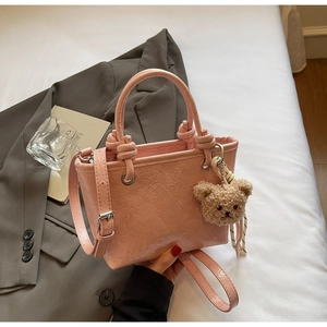 Detailed close-up of pink pleated leather bucket bag with a cute brown teddy bear charm