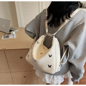 Detailed close-up of cream-colored backpack featuring metallic butterfly patches and texture