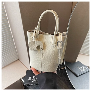 Macro view of cream litchi grain leather bucket bag with cute elephant charm detail