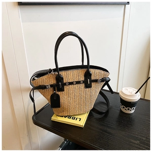 Detail of woven straw tote bag with black leather straps and metal eyelet accents