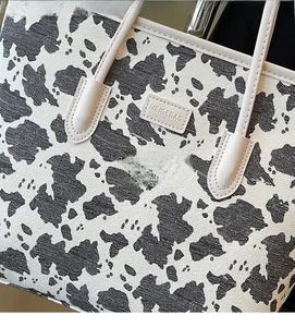 Detail of cow print tote bag with MEIGEBAG logo patch and cross-grain texture surface
