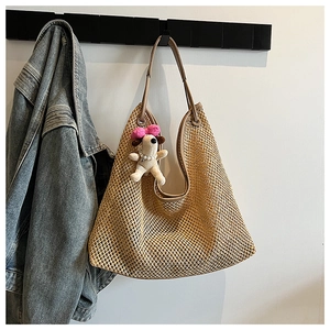 Detail of hollow woven straw tote bag featuring a cute plush puppy pendant and brown straps