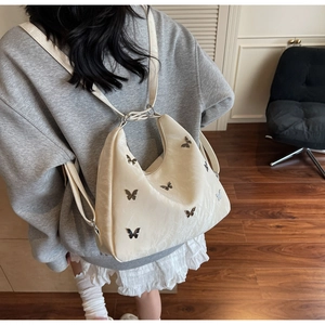 Detail view of a beige glossy shoulder bag with silver butterfly metal embellishments