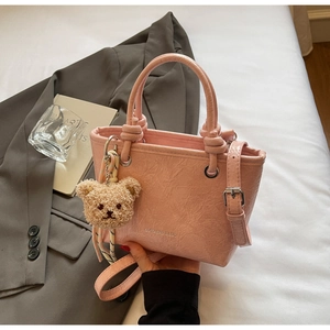 Detail of pink pleated bucket bag with brand logo and cute brown plush bear charm