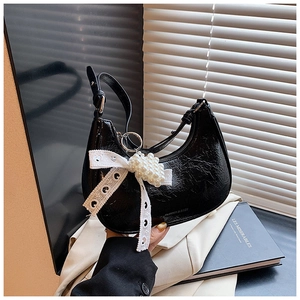 Detail of black pleated leather bag featuring white lace bow and pearl chain accessories
