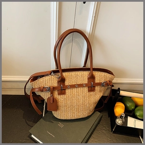Detail of woven straw tote bag featuring brown leather handles and a metallic buckle
