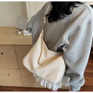 Detail of cream white pebbled leather bag with gold chain strap on model
