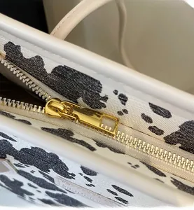 Detailed macro view of the smooth gold metal zipper and cow print texture on tote bag