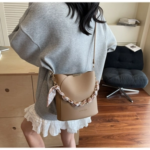 Détail du sac seau kaki avec bandoulière chaîne et foulard en soie sur un mannequin