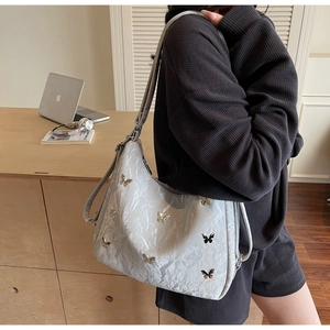 Detail of light blue pleated tote bag with silver butterfly charms on model shoulder
