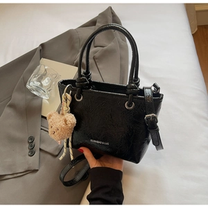 Detail of black wrinkled patent leather tote bag with shoulder strap and cute bear charm
