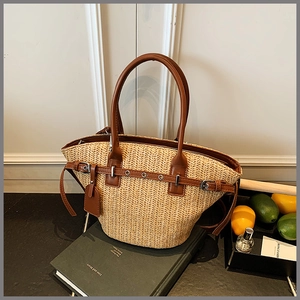 Detailed view of woven straw tote bag featuring brown leather trim and metal buckle accents