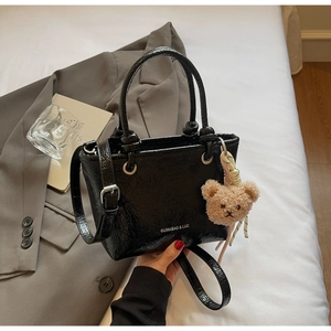 Detail of glossy black patent leather bucket bag with silver buckle and plush bear charm