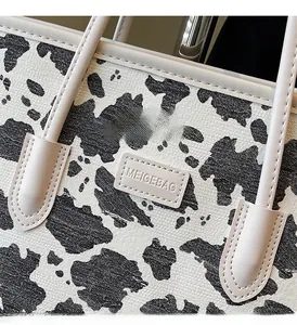 Close-up of the black and white cow print tote bag with a stitched logo patch