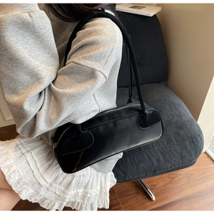Sleek black minimalist baguette bag with slim shoulder strap shown in a modern lifestyle setting