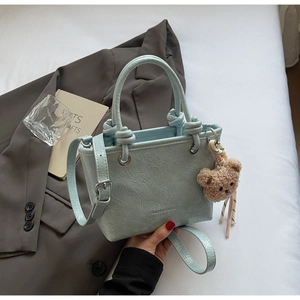Detail of mint green textured tote bag with knotted handle and brown plush bear charm