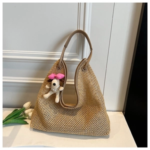 Detail of woven straw tote bag featuring brown faux leather handles and floral decor