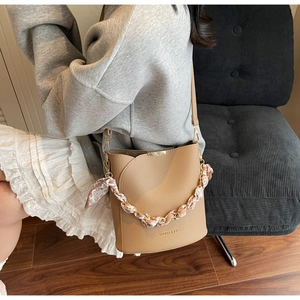Détail du sac seau en cuir marron avec chaîne en foulard de soie et métal doré